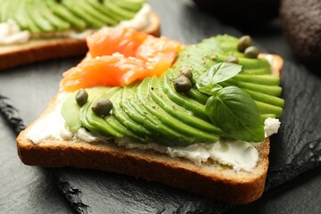 Delicious sandwiches with avocado, salmon, cream cheese, basil and capers on table, closeup