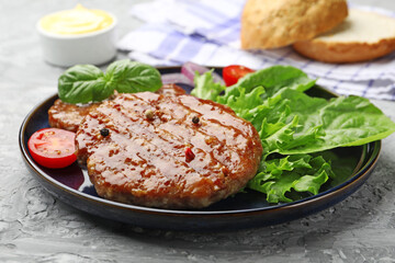 Delicious hamburger patties, tomato, lettuce, buns and spices on grey table, closeup