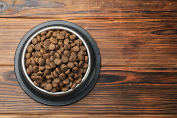 Dry pet food in feeding bowl on wooden background, top view. Space for text