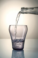 Pouring water from bottle into glass on mirror table against gray gradient background