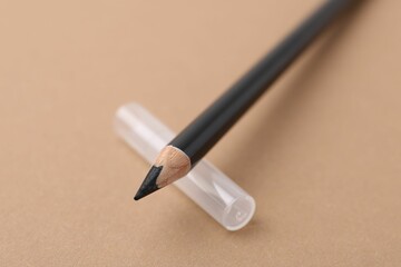Black eyebrow pencil on beige background, closeup