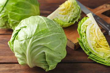 Fresh cabbages and knife on wooden table, closeup