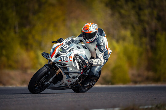  a person wearing a helmet, gloves, and shoes riding a 2018 BMW S1000RR on a race track, with trees in the background
