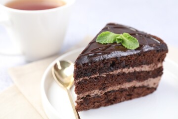 Piece of delicious chocolate cake, mint and spoon on light table, closeup