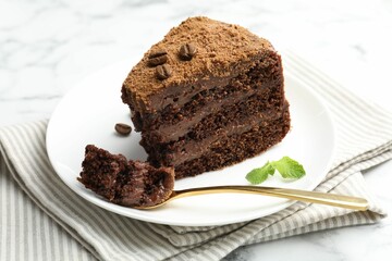 Piece of delicious chocolate cake with coffee beans, mint and fork on light table, closeup