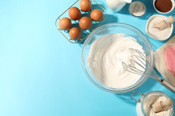 Whisk with whipped cream, eggs and other products on light blue table, flat lay. Space for text