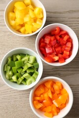 Pieces of fresh colorful bell peppers in bowls on wooden table, flat lay