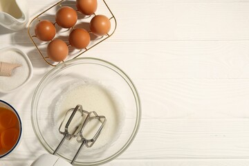 Hand mixer, egg whites in bowl, eggs and other products on white wooden table, flat lay. Space for text