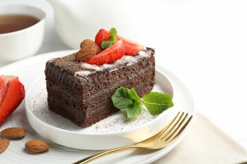 Piece of delicious chocolate cake with strawberries, almonds, mint and tea on table, closeup