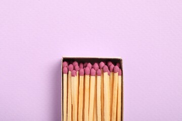 Matches in open box on violet background, top view. Space for text