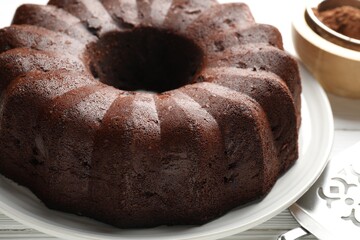 Tasty chocolate bundt cake, cocoa powder and server on table, closeup