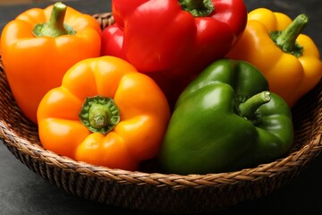 Fresh colorful bell peppers in wicker basket on dark table, closeup