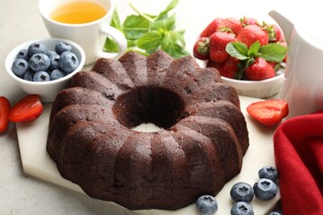 Tasty chocolate bundt cake, tea and berries on light table, closeup