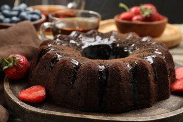 Tasty chocolate bundt cake with glaze, tea and berries on wooden table, closeup