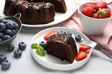Piece of delicious chocolate bundt cake with strawberries, mint and blueberries on light grey textured table, closeup