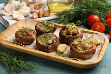 Delicious stuffed mushrooms with melted cheese, garlic and dill on light blue wooden table, closeup