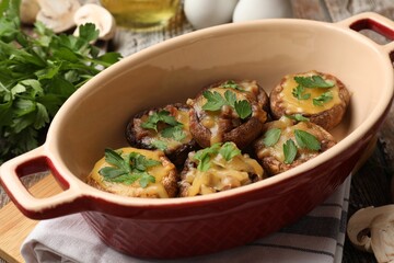 Delicious stuffed mushrooms with melted cheese and parsley in baking dish on table, closeup