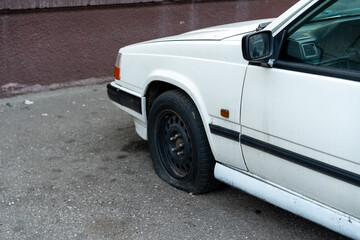 Flat tire on a white car parked near a brown wall in an urban setting during the day