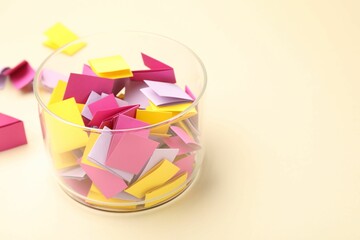 Jar with colorful pieces of paper on beige background, closeup. Space for text