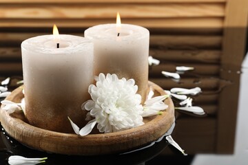 Burning candles and beautiful flowers on wet black mirror surface, closeup