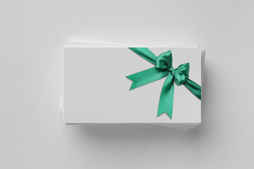 Blank gift card with green bow on light grey background, top view. Mockup for design