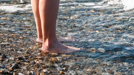 Girl on pebble beach went into water, summer evening, view from below, vacation, rest