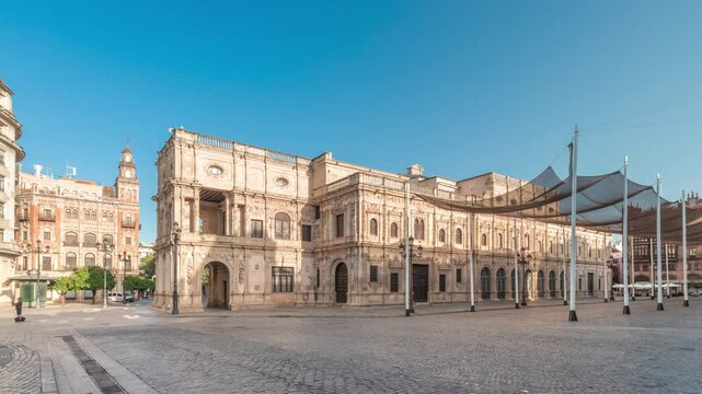 Panorama showing morning timelapse of the Town Hall in Plaza de San Francisco, Seville. Casa Consistorial, Plateresque architecture surrounded by traditional Andalusian buildings under a blue sky