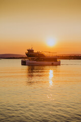 Fototapeta premium Bathed in the golden light of sunset, a local ferry glides across Oslo harbour, creating a warm and inviting scene against the city's waterfront