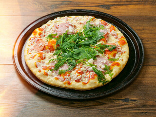 A pizza with ham and spinach on a black tray. The pizza is sitting on a wooden table. Fine Italian cuisine with fresh ingredients ready to be cooked. Fast food meal.