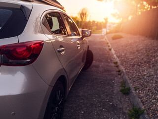 Small car parked by a house with white walls, country side in the background with sunset glowing and flare. Calm light and airy look, selective focus. Living in rural area concept. Nobody