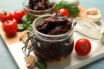 Delicious sun dried tomatoes, fresh vegetables, basil and garlic on blue wooden table, closeup