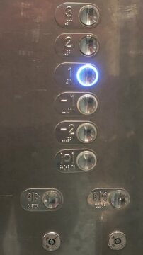 Modern elevator interior with hand pressing illuminated ground floor button on sleek metallic control panel, highlighting accessibility and urban transportation technology