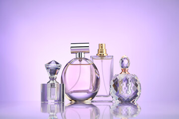 Bottles of perfume on mirror surface against violet gradient background