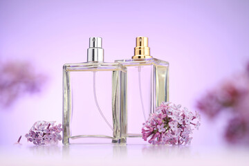 Bottles of perfume and lilac flowers on mirror surface against violet gradient background,...