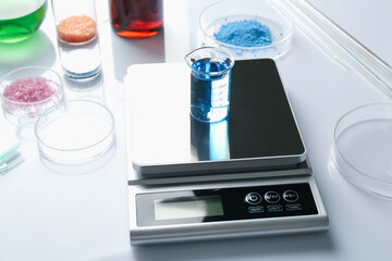 Scale with beaker of sample and other laboratory equipment on white background, closeup