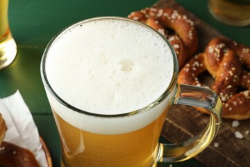 Glass of beer and tasty pretzels on green table, selective focus