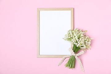 Beautiful lily-of-the-valley flowers and blank frame on light pink background, top view. Space for text