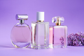 Bottles with perfumes and lilac flowers on purple gradient background, closeup