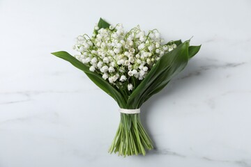 Bouquet of beautiful lily-of-the-valley flowers on white marble background, top view