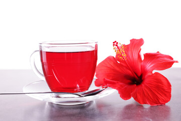 Tasty hibiscus tea in cup, spoon and beautiful flower on grey textured table against white background