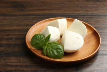 Pieces of delicious mozzarella cheese and basil on wooden table, closeup