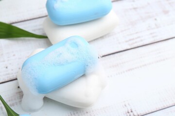 Soap bars with foam on white wooden table, above view. Space for text