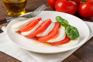 Tasty mozzarella, tomatoes, oil and basil on wooden table, closeup