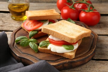 Tasty sandwiches with mozzarella cheese, tomatoes and basil on wooden table, closeup