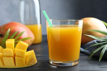 Tasty mango juice in glass, fresh fruits and green leaves on wooden table, closeup