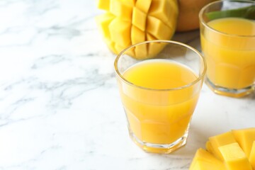Tasty mango juice in glasses and fresh fruits on white marble table, closeup. Space for text