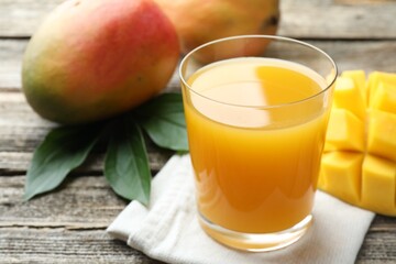 Tasty mango juice in glass, fresh fruits and green leaves on wooden table, closeup