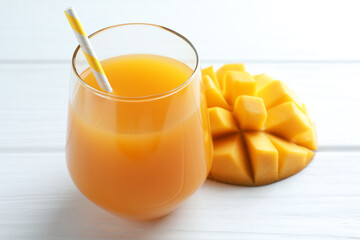 Tasty mango juice in glass and fresh fruit on white wooden table, closeup
