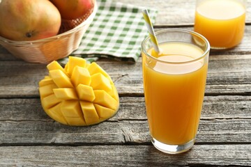 Tasty mango juice in glass and fresh fruits on wooden table, closeup