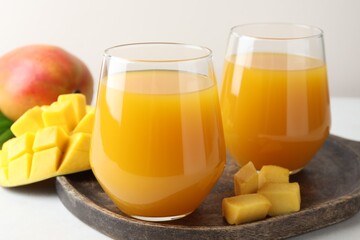 Tasty mango juice in glasses and fresh fruits on white table, closeup